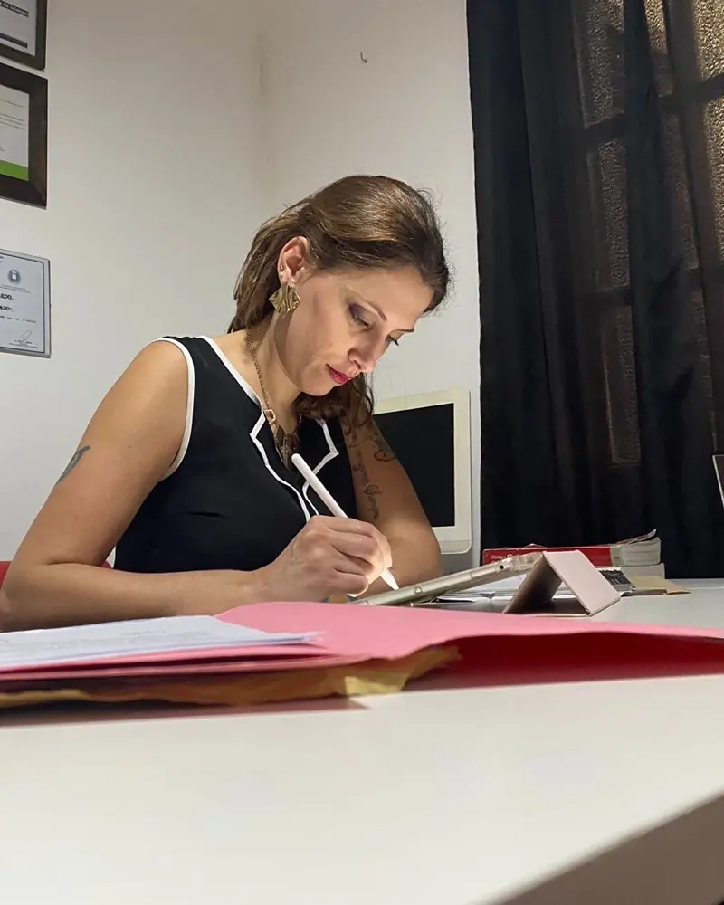 Noelia D. Lombardo escribiendo en su escritorio, entre carpetas de expedientes